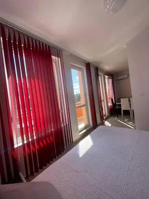 a bedroom with a large window with red blinds at A Tiny Flat in Sunny Beach