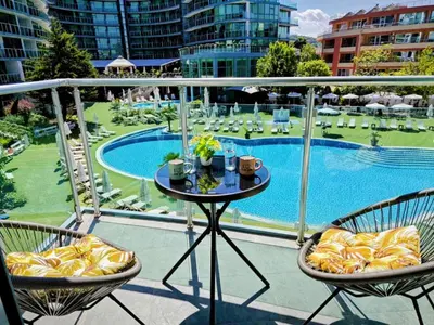a balcony with a table and chairs and a pool at Sunny Cozy Apartment Primorsko in Primorsko