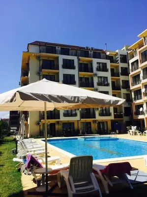 a pool with chairs and an umbrella next to a building at SannyBeach AmberBeach Apartment Bulgaria A14-1 in Sunny Beach