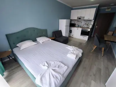 a bedroom with a bed with white sheets and a kitchen at Apartments in Panorama Beach Vigo Nessebar in Nesebar