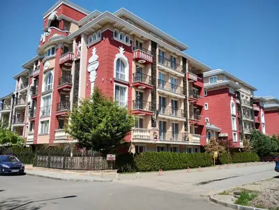 a red apartment building with a car parked in front of it at Apartament Messambria Resort - Bastet BS in Sunny Beach