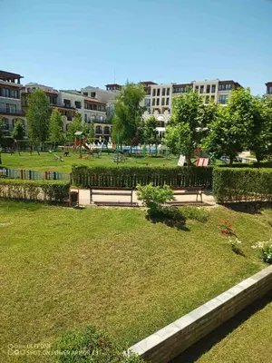 a park with benches in the grass with buildings in the background at Апартамент Blue в местност Каваци, Созопол in Sozopol
