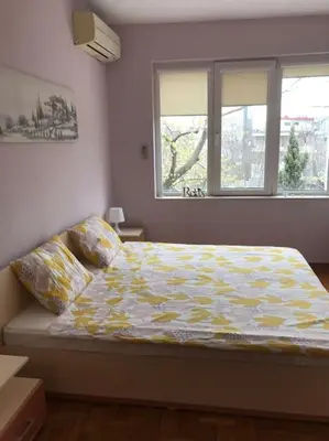a bedroom with a bed with a yellow comforter and two windows at Star Ray Apartment in Varna City