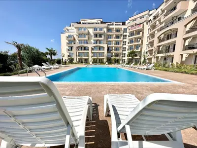 a swimming pool with white chairs and a building at Ipanema Beach - Menada Apartments in Sveti Vlas