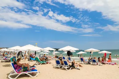 a group of people sitting on a beach with umbrellas at Luxury First Line apartment with pool and sea view in complex Oazis in Ravda