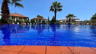a large blue swimming pool with palm trees in the background at Bratanov Cascadas Ravda in Ravda