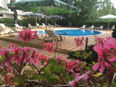 a swimming pool with chairs and umbrellas and pink flowers at Beatris Family House in Sunny Beach