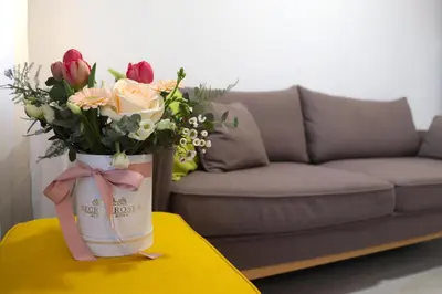 a vase of flowers on a table in front of a couch at Апартамент МАРГО in Burgas City