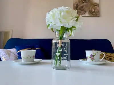 a glass vase with white flowers on a table with two cups at Apartament Esperanza in Sunny Beach