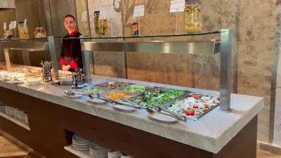 a woman standing behind a buffet line of food at St. Sofia Beach Hotel in Kiten