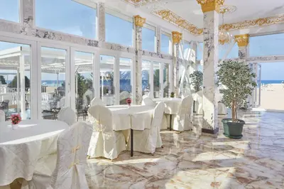 a dining room with white tables and chairs and windows at Hotel Amore Beach - All Inclusive in Elenite