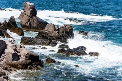 a person sitting on some rocks in the ocean at Hotel Gamartata in Duni