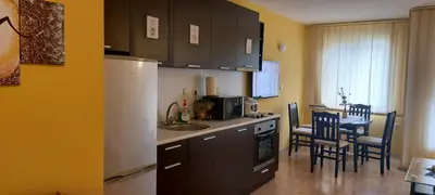 a kitchen with brown cabinets and a table with chairs at Илеа апартамент in Burgas City