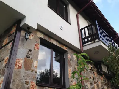 a house with black windows and a stone wall at Zapovedni Rai in Primorsko