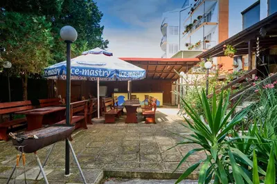 a patio with tables and an umbrella and benches at Hotel Koral in Primorsko
