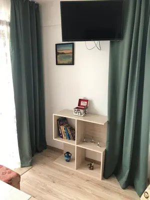 a book shelf with a television on a wall with green curtains at Guest House Liliya in Sozopol