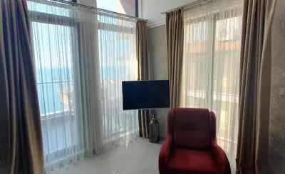 a living room with a red chair and large windows at Апартамент Злато изглед МОРЕ in Sozopol