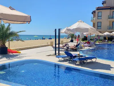 a swimming pool next to a beach with people lounging on chairs at Apartments Obzor Beach B - Апартаменти Обзор Бийч B in Obzor