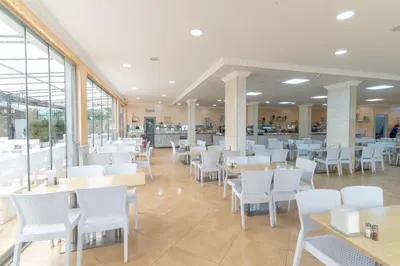 a restaurant with white chairs and tables and windows at Hotel Riva - All Inclusive in Sunny Beach