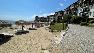 a beach with straw umbrellas and chairs and the ocean at Studio in Garden of Eden D402 - Sveti Vlas, Bułgaria in Sveti Vlas