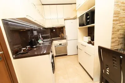 a kitchen with white cabinets and a white refrigerator at Апартамент за гости Уют in Burgas City