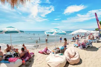 a group of people sitting on a beach with umbrellas at Premier Fort Apartment on Seafront in Sveti Vlas