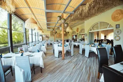 a restaurant with white tables and chairs and windows at Хотел и Вили Марая in Tsarevo