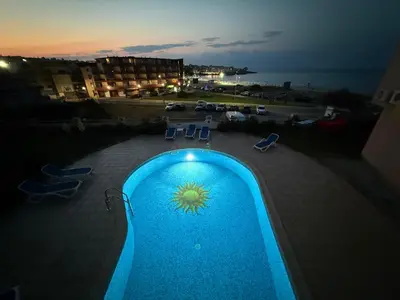 a blue swimming pool with chairs and a view of the ocean at Black Pearl Apartment in Sozopol