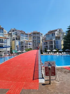 a red walkway leading to a swimming pool with buildings at Апартамент Бриджит Слънчев бряг in Sunny Beach
