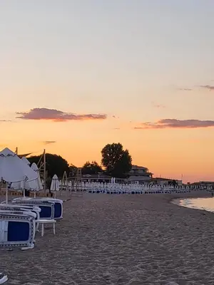 a beach with chairs and umbrellas at sunset at Апартамент Бриджит Слънчев бряг in Sunny Beach