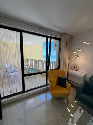 a living room with a yellow chair and a balcony at Gold Coast SP apartments in Burgas City
