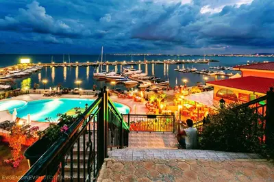 a man sitting next to a swimming pool at a marina at Helios Seaview Apartment in Sveti Vlas