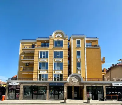 a tall yellow building with a clock on it at Triumph apartment in Burgas City