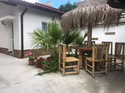 a patio with a table and chairs under a straw umbrella at Вила Оазис Сарай - Царево in Tsarevo