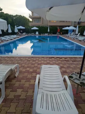 a large swimming pool with white chairs and umbrellas at Kamelia Garden Apartment in Sunny Beach