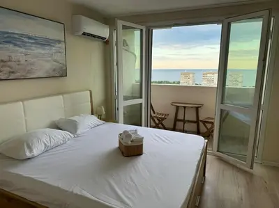 a bedroom with a bed with a view of the ocean at Апартамент Панорама Лазур in Burgas City
