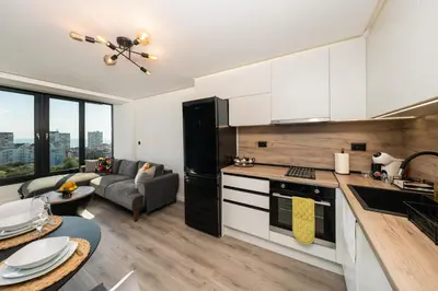 a kitchen with white cabinets and a living room at Lazur Sea View in Burgas City