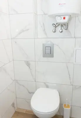 a white bathroom with a toilet and a white tiled wall at Bright 2-Bedroom Apartment Near Varna City Center by Flat Mаnаger in Varna City
