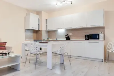 a kitchen with white cabinets and a white table and chairs at АТ apartment - Pool View in Varna City