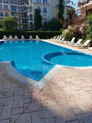 a large blue swimming pool with chairs and a building at Просторная квартира в популярном комплексе in Sunny Beach