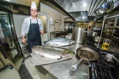 a chef standing in a kitchen with three fish at Premier Fort Cuisine - Full Board in Sunny Beach