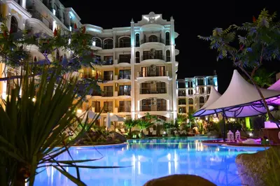 a large hotel with a swimming pool at night at Harmony Suites - Monte Carlo in Sunny Beach