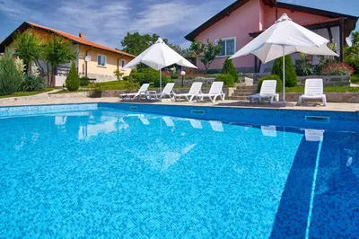 a swimming pool with chairs and umbrellas next to a house at BulgariaVilla - Royal Villas in Bryastovets