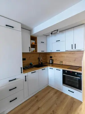 a white kitchen with white cabinets and a wooden floor at Апартамент BLUE CREAM in Burgas City
