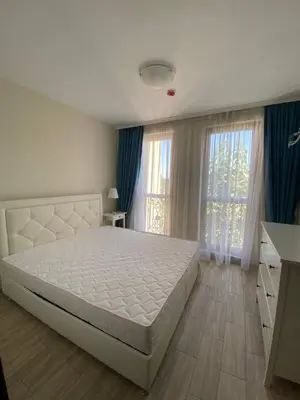 a bedroom with a large white bed and blue curtains at Апартамент Cascadas in Sunny Beach