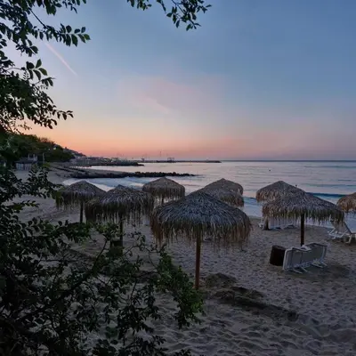 a beach with some straw umbrellas and the ocean at Villa Sardinia Sveti Vlas Studio in Sveti Vlas
