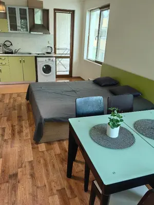 a bedroom with a bed and tables and a kitchen at Уютно студио в Поморие Мари in Pomorie