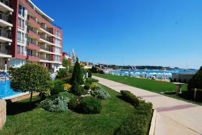 a garden in front of a building next to the water at Aurelia Beach Complex in Ravda