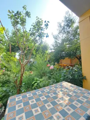 a tiled table in a garden with trees and bushes at Family Hotel Magnolia - Summer residence in Primorsko