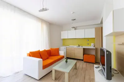 a living room with an orange couch and a kitchen at APOLONIS hotel in Sozopol